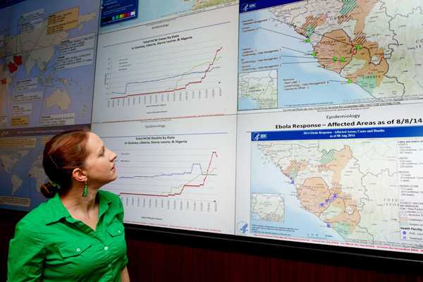 Photo: CDC Disease Detective Molly stands near the electronic information wall in the CDC’s Emergency Operations Center in Atlanta.