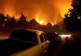 Cars along wildfire evacuation route. Wildfire in the background. 