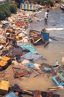 Boy standing next to debris in the water along a river shore