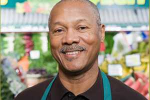 older man wearing an apron in a produce aisle of a grocery store