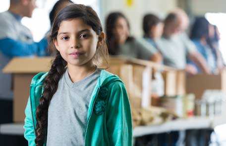 Young girl standing in front of people packing boxes