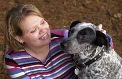 This photograph depicts an unidentified mixed breed dog, sometimes referred to as a mutt, seated along side its master. Note the docile, relaxed disposition of this pet, which is ideal when thinking about adding a canine family member.