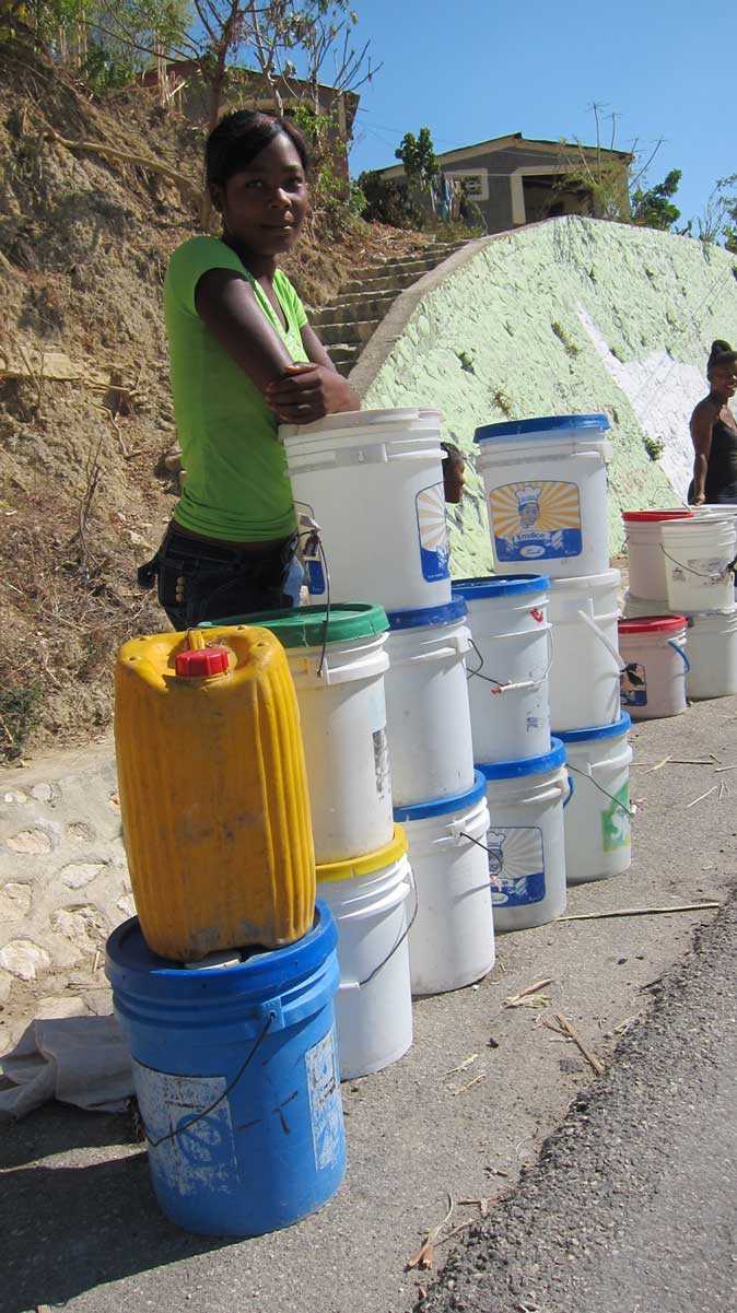 Trianon, Haiti - A community member gathers water from a spring in the village of Trianon as staff members of DINEPA (the National Directorate for Drinking Water and Sanitation) test the water for chlorination. With CDC support, 54 of the 270 Drinking Water and Sanitation Technicians (TEPAC's by their French acronym) across Haiti who work for DINEPA are equipped with motorcycles and testing equipment, as well as have their salaries covered.