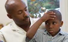 African American boy with holding his forehead while sitting on his father's lap