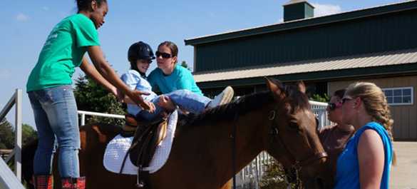 Volunteers help a rider onto one of the horses at Storybook Farm