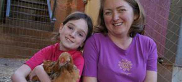Young girl sits with her mom, holding her pet hen.