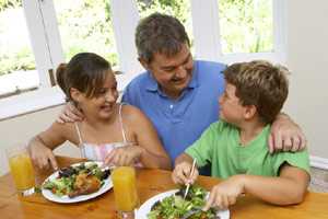 	photo of 2 kids and man eating salad and baked chicken