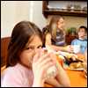  girl drinking a glass of milk, with her family in the background