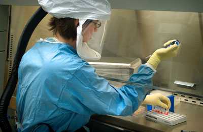 Laboratorian works with test tubes at a fume hood wearing personal projective equipment.