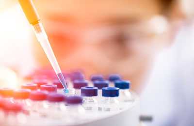 Scientist using a pipette to insert liquid into vials.