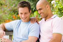 MSM couple sitting on a park bench, smiling, and drinking coffee.