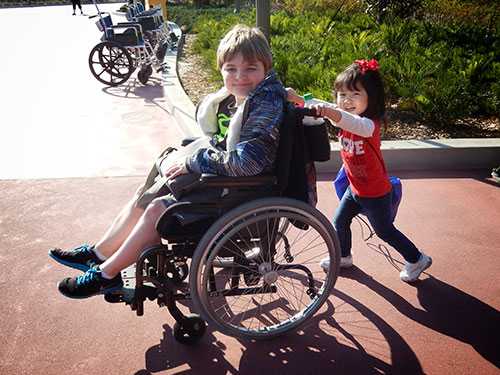 A little girl pushing her brother in a wheelchair