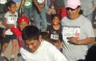 A large group of American Indian children and adults wear bike helmets and pose with two bikes