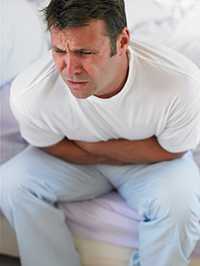 Photo of a man doubled over in bed grabbing his stomach.