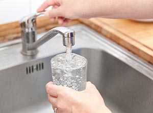 Photo of a woman getting a glass of water from kitchen faucet.