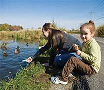 Mother and daughter feeding ducks on a roadside pond