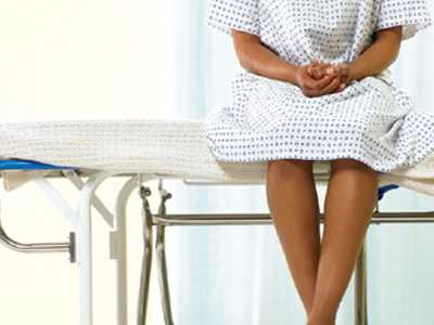 	Patient sitting in a hospital gown on a wheeled gurney, bare feet dangling. White walls and white floors.