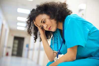 Healthcare worker sitting with her hand on her head.