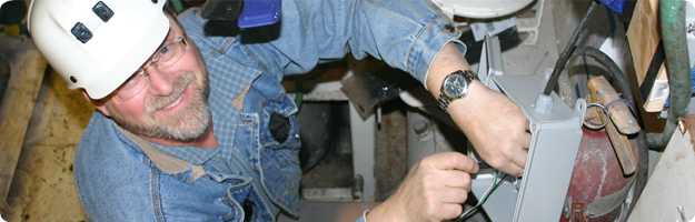 	A close up photo taken from above of a NIOSH researcher installing a hatch and door monitor sensor in the engineering space of a Bering Sea trawl vessel.