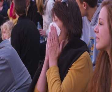 Woman in the stands at a football game covering her cough with a tissue.