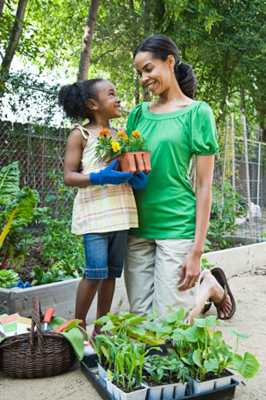 mom helping daughter plant flowers with gloves on