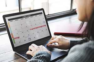 Lady sitting with laptop looking at monthly calendar