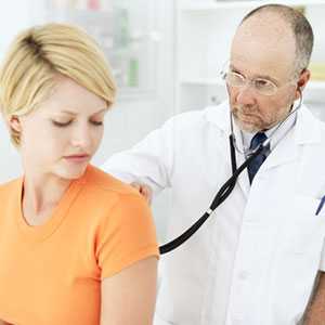 A doctor examines a college-aged woman with a stethoscope