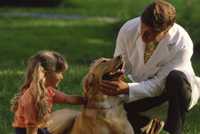 man in white lab coat with a girl looking at a dog