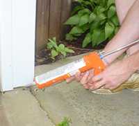 Person using caulk gun to seal holes on exterior of house