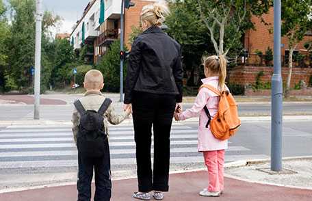 	Madre a punto de cruzar la calle con sus hijos de la mano