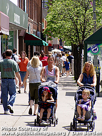 Two women push strollers along a busy pedestrian sidewalk in East Lansing, MI.