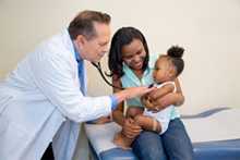 Doctora examinando una niña; madre sonriente