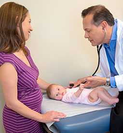 Mother smiles as doctor with stethoscope listens to her baby’s heartbeat.