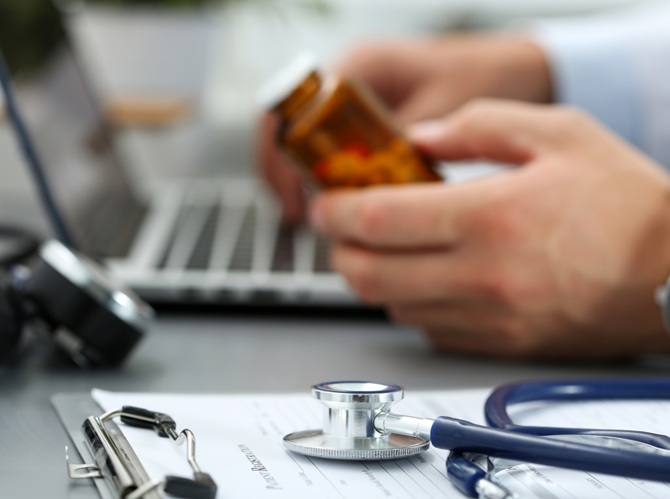 Stethoscope on clipboard with doc holding pill bottle