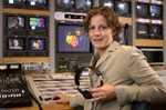 Woman sitting next to mixing board and tv's